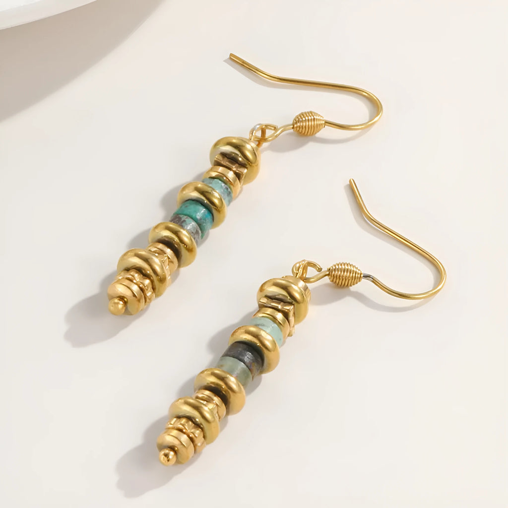 A pair of geometric-shaped, gold-toned dangle earrings on a plain background.