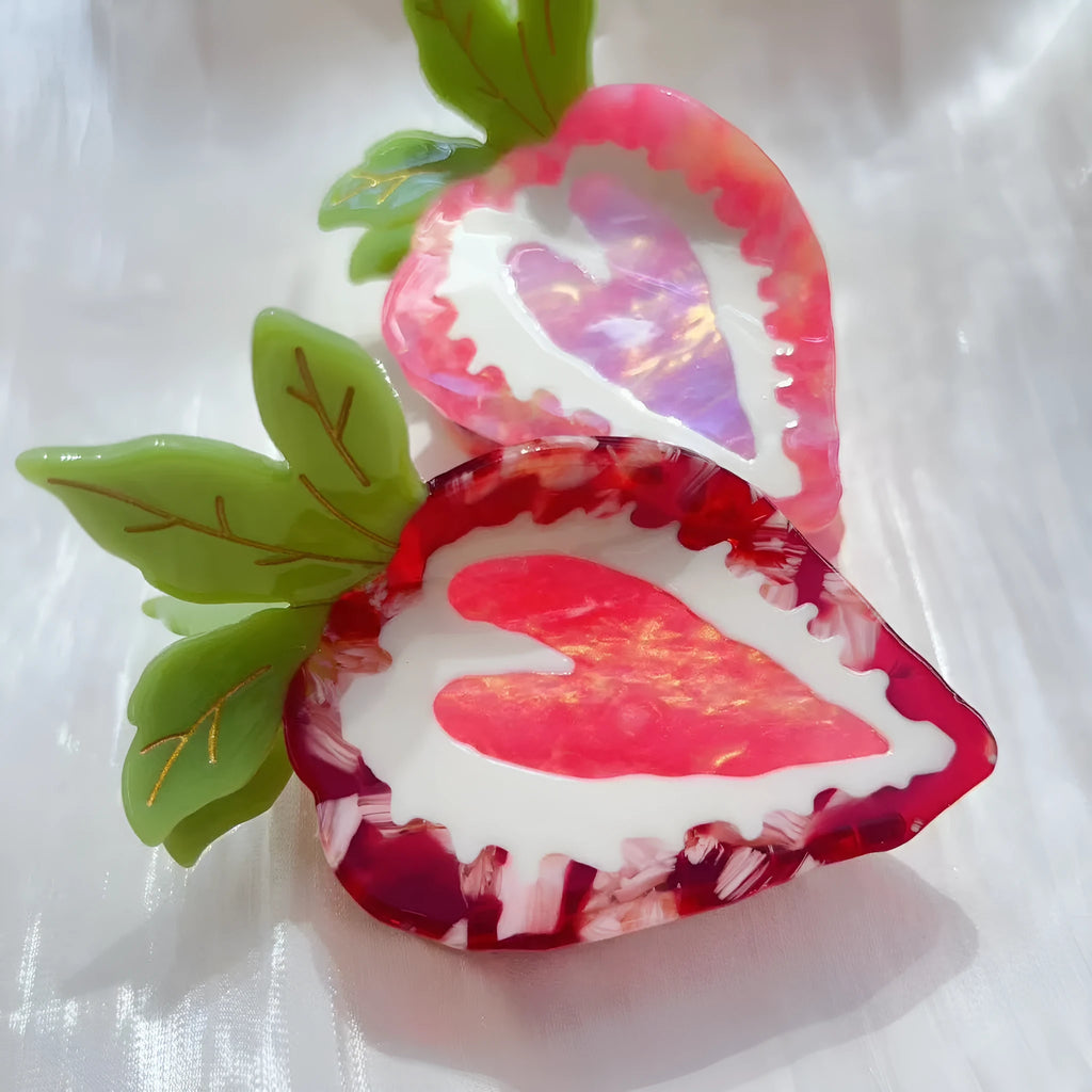 Close-up of a red strawberry-shaped hair clip with a green leaf, on a white background.