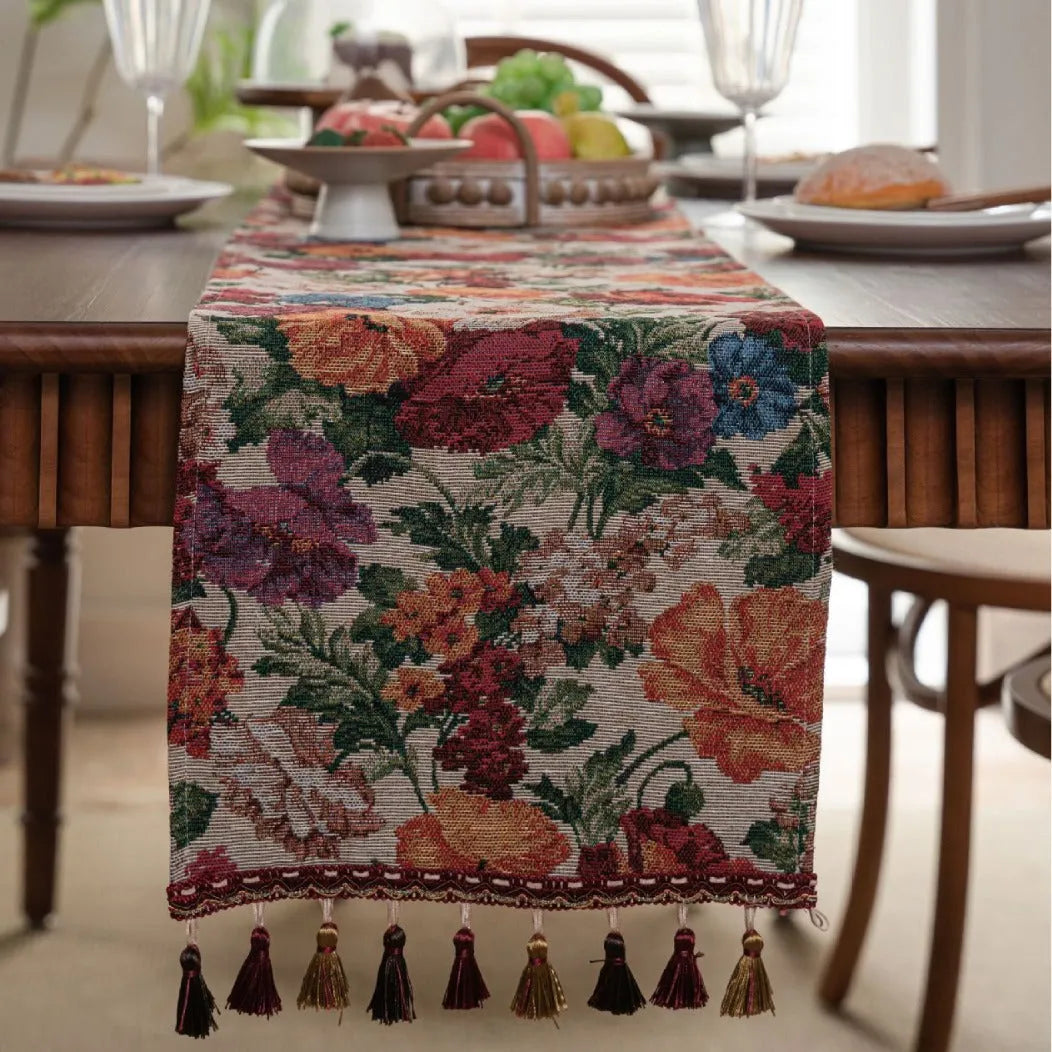 Beige jacquard table runner with floral pattern and long tassels laid on a wooden table.