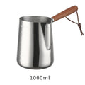 Stainless steel milk jug with wooden handle and internal measuring scale for barista coffee art.