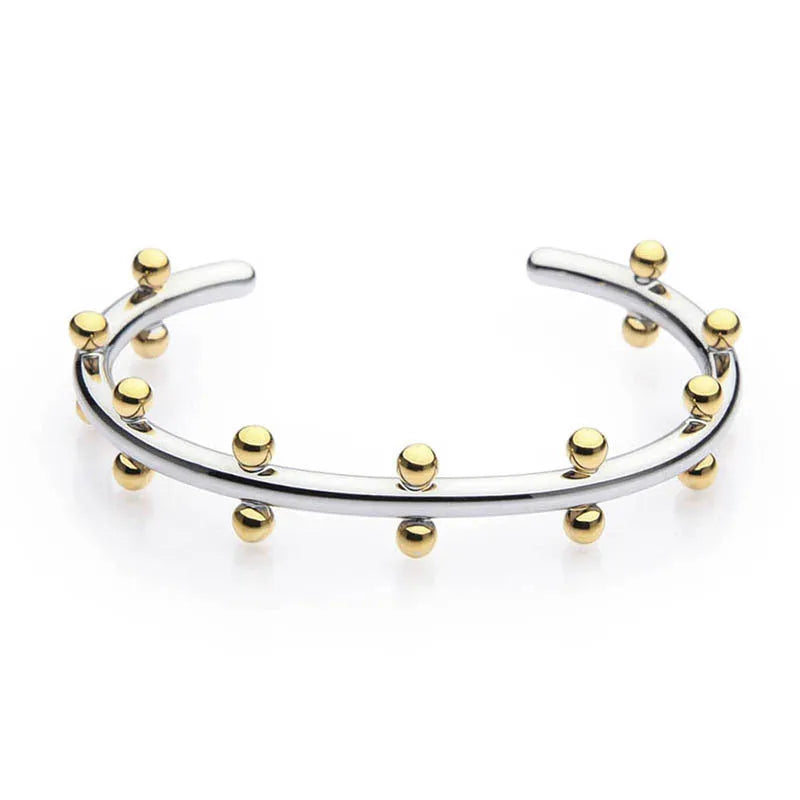 Close-up of textured stainless steel C-shaped bean bead charm in gold finish, shown next to an alloy bracelet.
