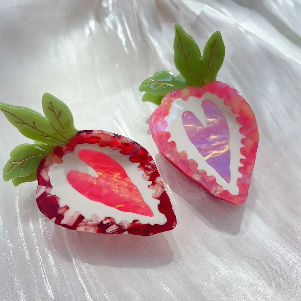 Close-up of a red strawberry-shaped hair clip with a green leaf, on a white background.
