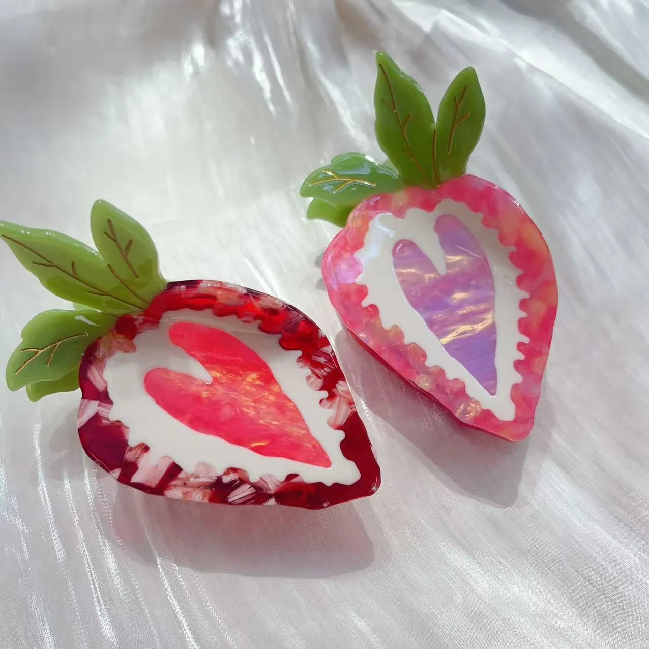 Close-up of a red strawberry-shaped hair clip with a green leaf, on a white background.