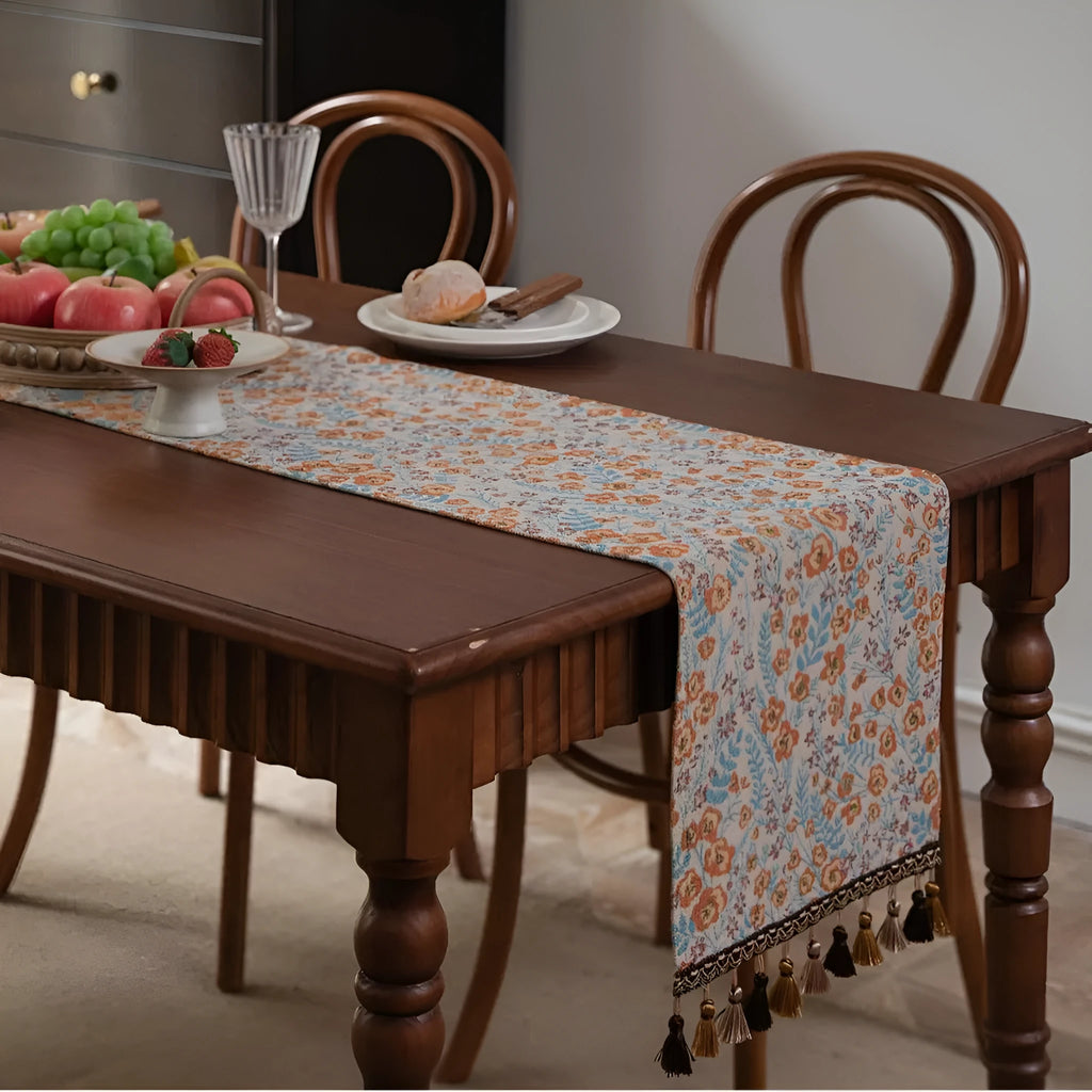 Beige jacquard table runner with floral pattern and long tassels laid on a wooden table.