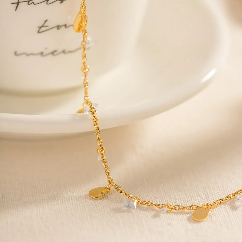Close-up of a women's stainless steel anklet with a water drop pendant and tassel detail.
