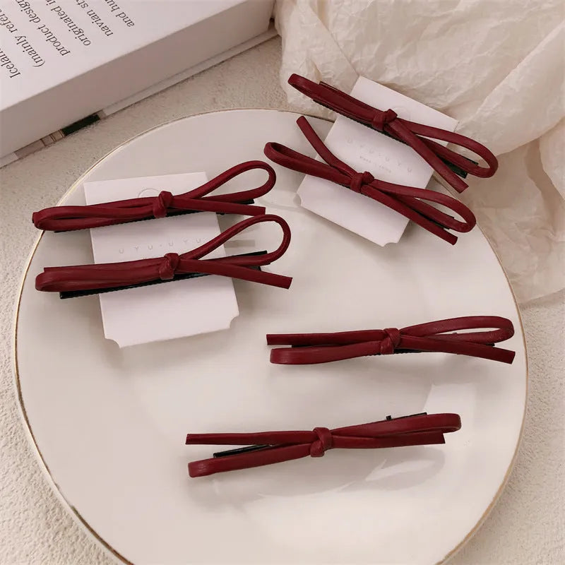 Wine red leather bow hair barrettes shown from multiple angles on dark background