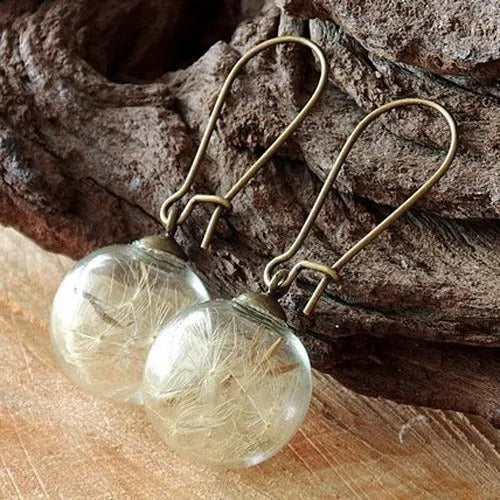 Close-up of transparent glass ball earring with crystal dandelion seed design on a silver hook.