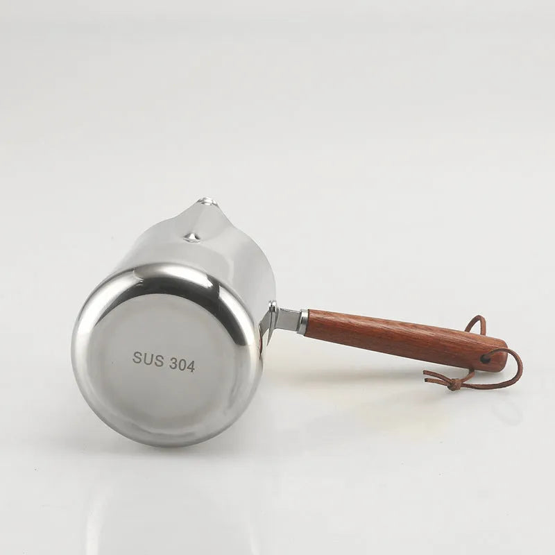 Stainless steel milk jug with wooden handle and internal measuring scale for barista coffee art.