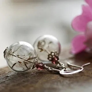 Close-up of transparent glass ball earring with crystal dandelion seed design on a silver hook.