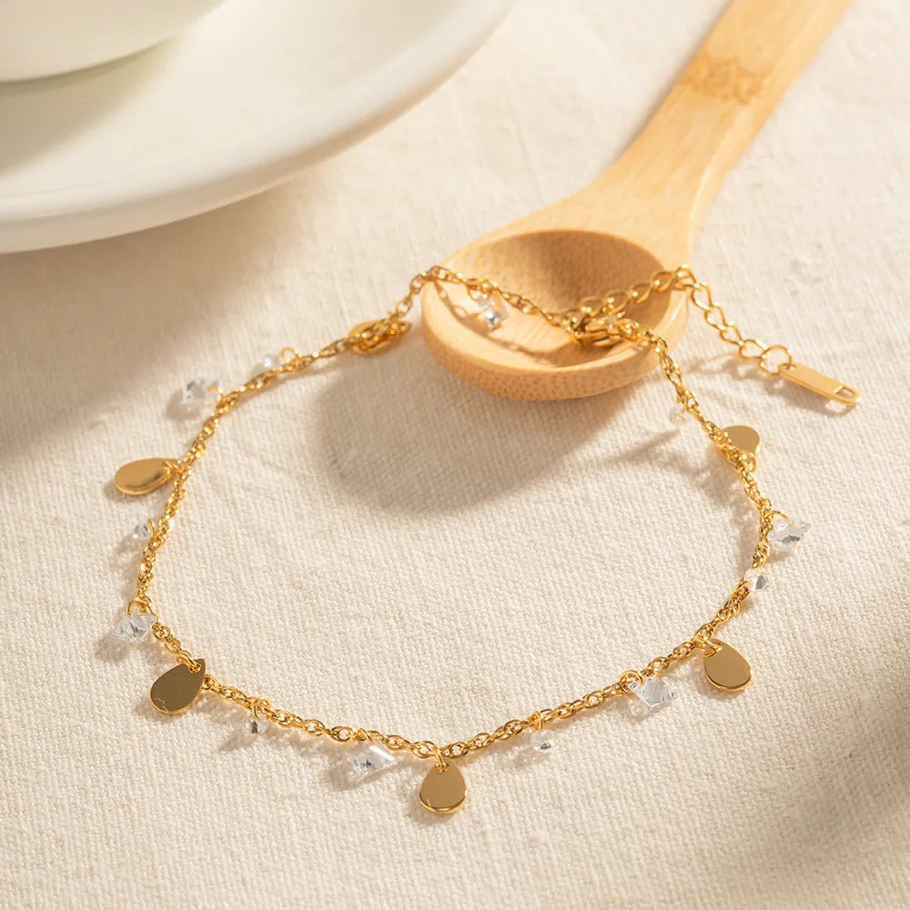 Close-up of a women's stainless steel anklet with a water drop pendant and tassel detail.