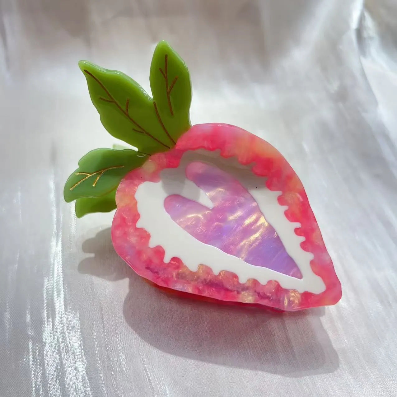 Close-up of a red strawberry-shaped hair clip with a green leaf, on a white background.
