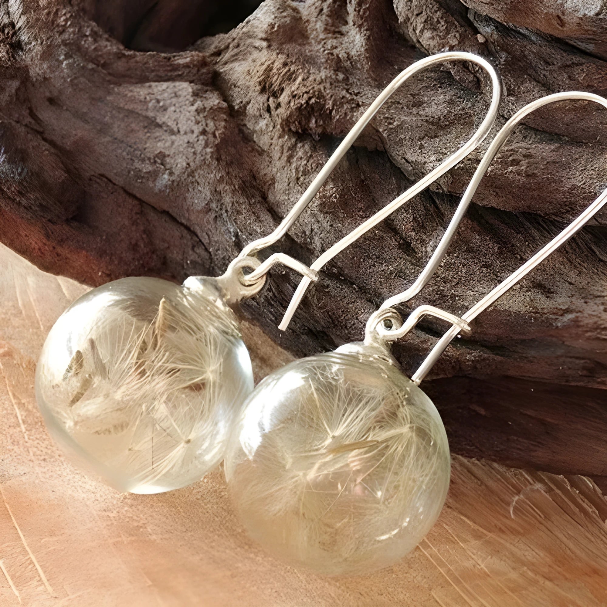 Close-up of transparent glass ball earring with crystal dandelion seed design on a silver hook.