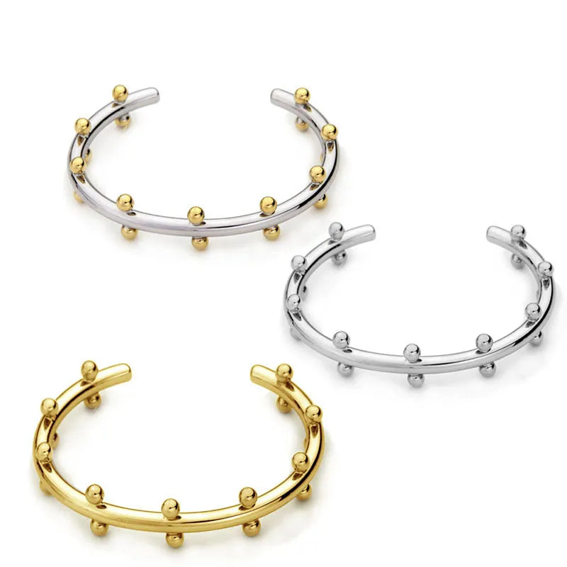 Close-up of textured stainless steel C-shaped bean bead charm in gold finish, shown next to an alloy bracelet.