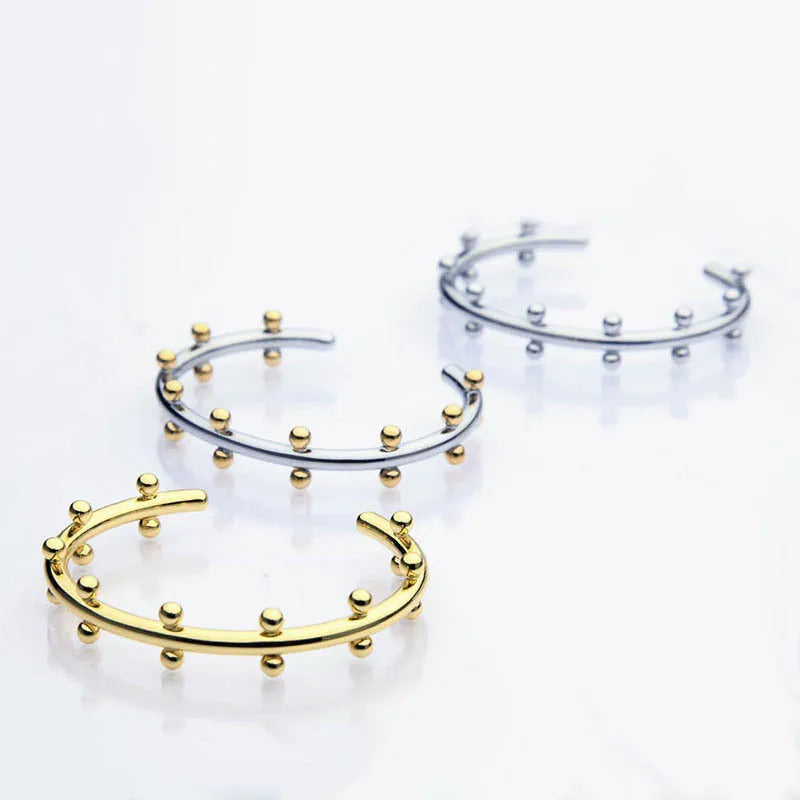 Close-up of textured stainless steel C-shaped bean bead charm in gold finish, shown next to an alloy bracelet.