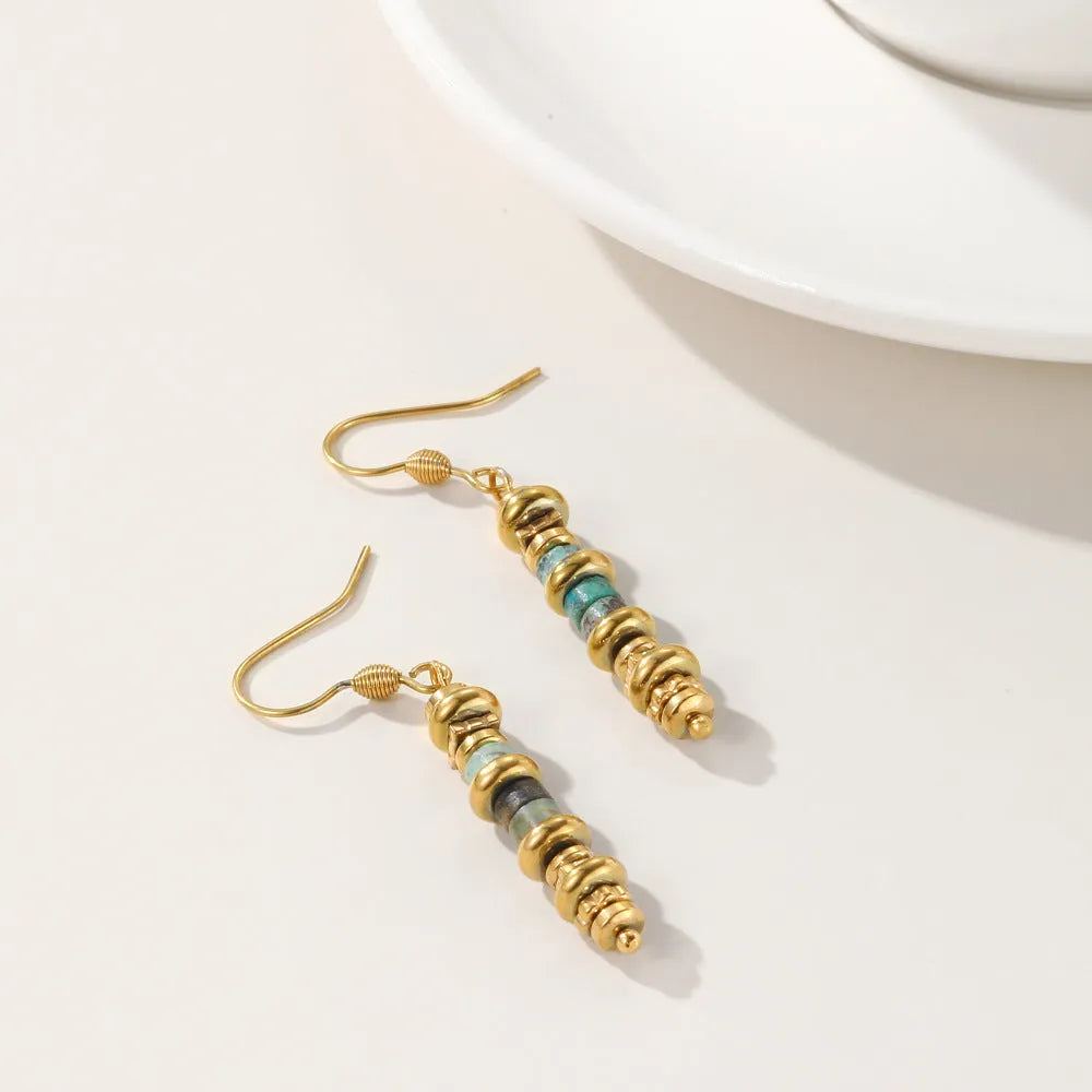 A pair of geometric-shaped, gold-toned dangle earrings on a plain background.