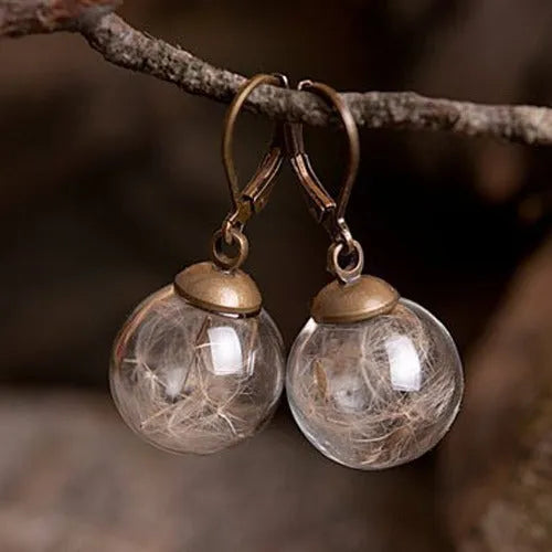 Close-up of transparent glass ball earring with crystal dandelion seed design on a silver hook.
