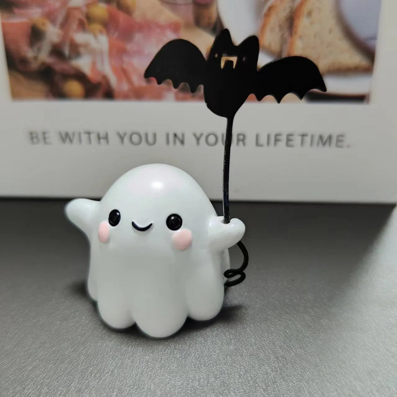 Miniature resin statue of a white ghost dog walking and holding a small black bat, Halloween decoration.