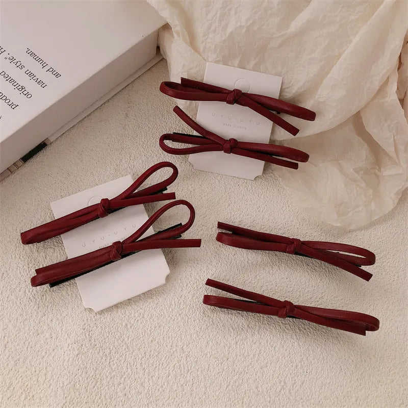 Wine red leather bow hair barrettes shown from multiple angles on dark background