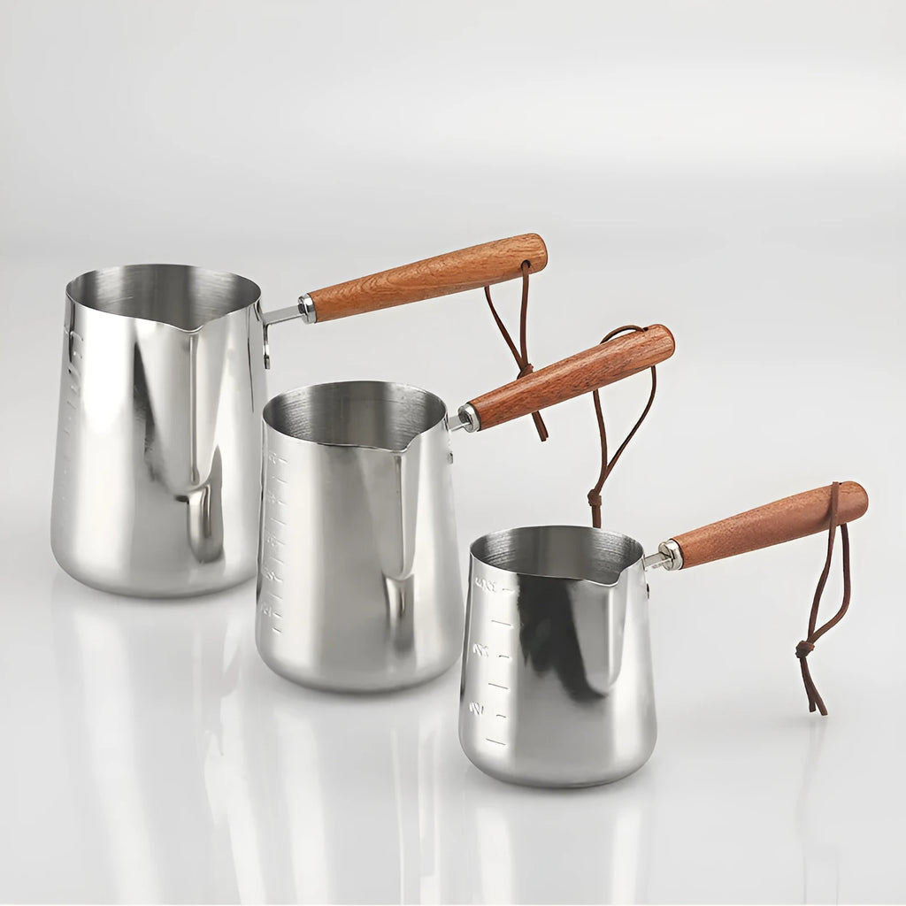 Stainless steel milk jug with wooden handle and internal measuring scale for barista coffee art.