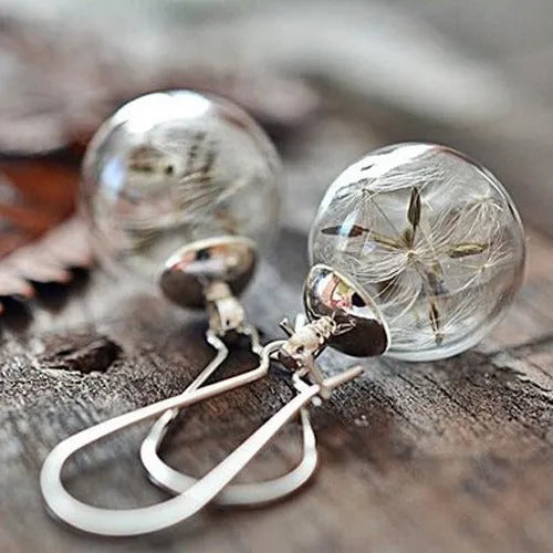 Close-up of transparent glass ball earring with crystal dandelion seed design on a silver hook.