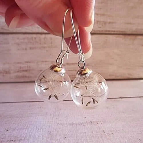 Close-up of transparent glass ball earring with crystal dandelion seed design on a silver hook.