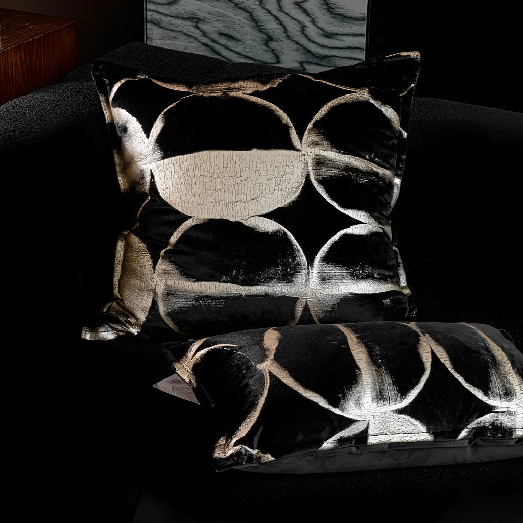Black and gold abstract pattern decorative flannel pillow with removable cover on a grey sofa.