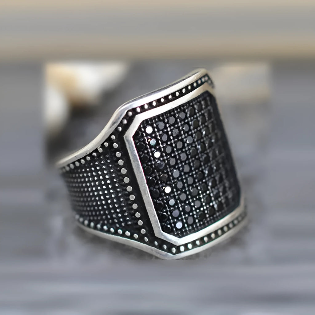 Close-up of a black alloy ring with a zircon stone and copper-coloured inlay detailing on the band.