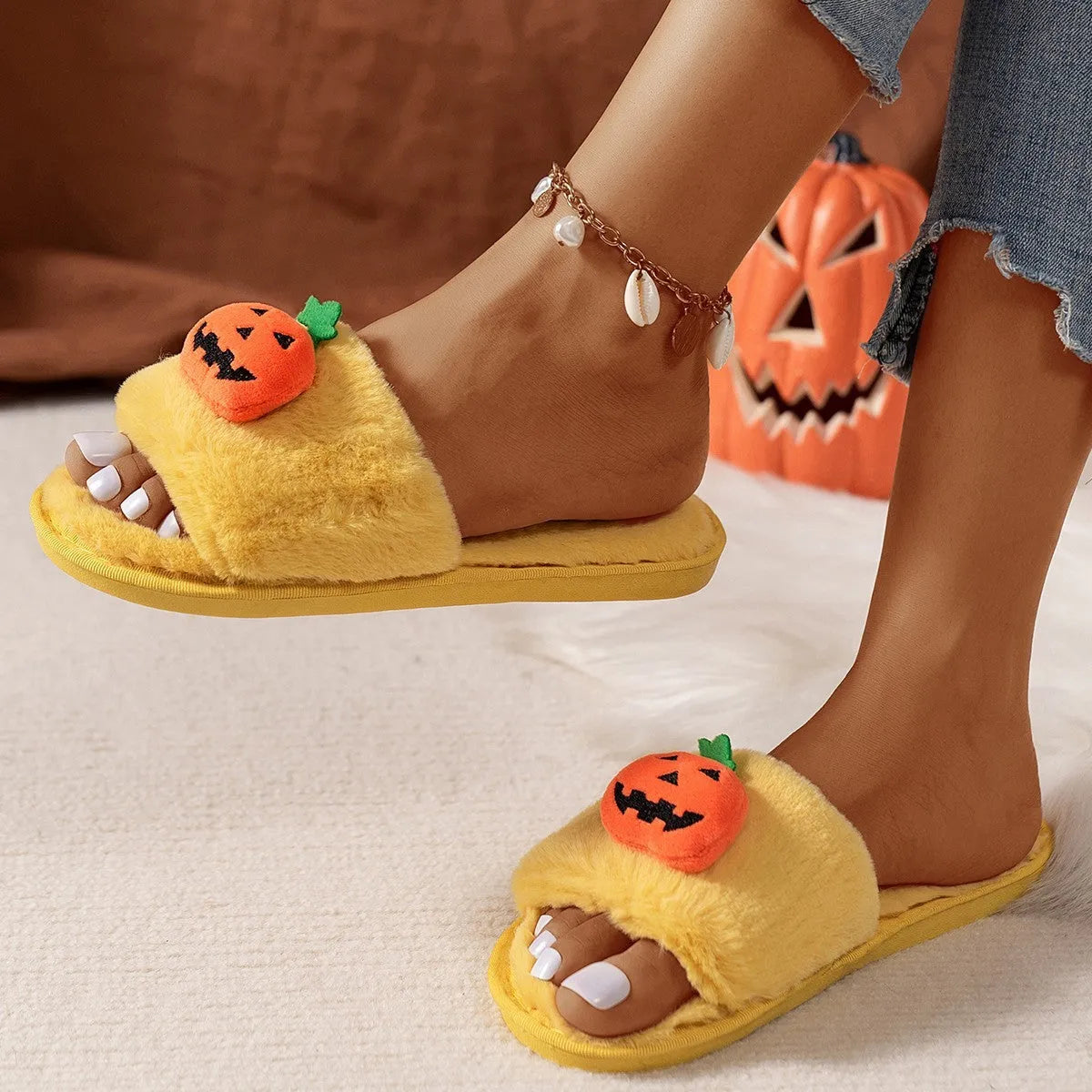 Yellow pumpkin plush open-toe slippers with a cartoon face, shown on a white background.