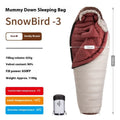 Blue and grey mummy-style sleeping bag with compression sack on a pine forest floor.