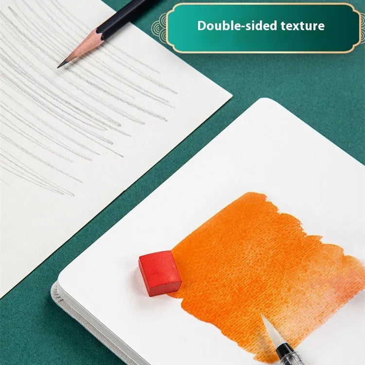 Feiluniao fabric-covered watercolour notebook open on a table with art supplies.