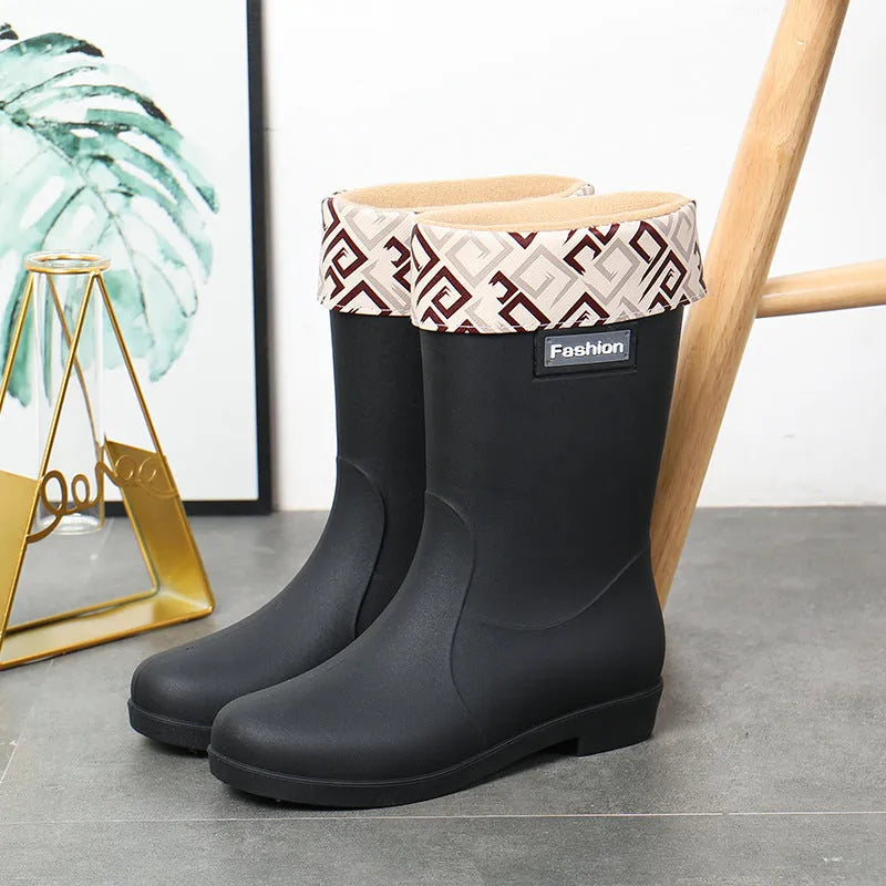 Women's black PVC mid-calf rain boot with a low heel on a wet surface.