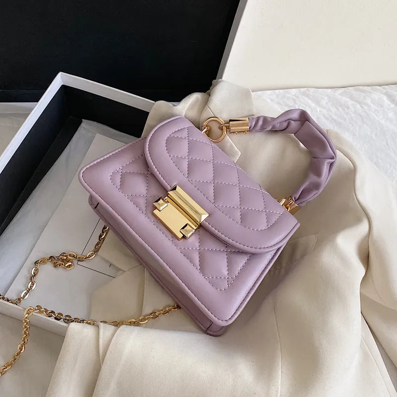 Purple soft PU leather small square shoulder bag with a long strap on a table.