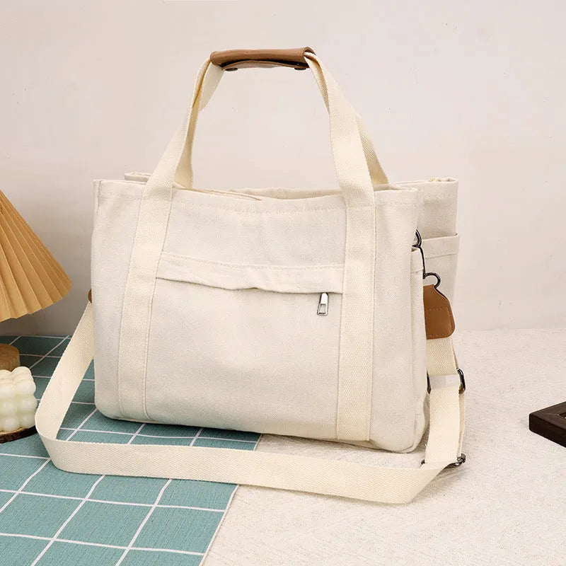 Large horizontal square canvas tote bag with crossbody strap and multiple internal pockets.
