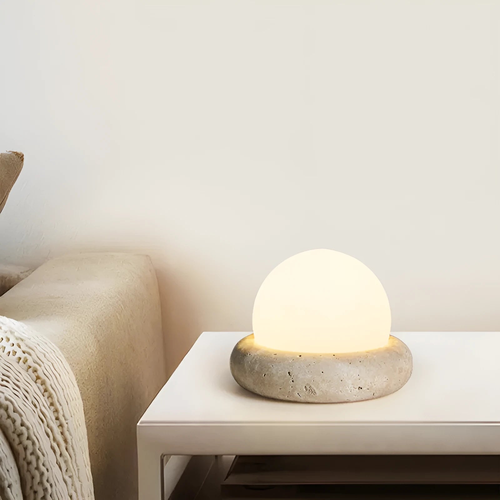 Cream coloured spherical bedside night lamp with remote control on wooden table