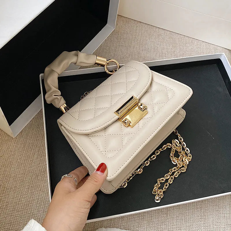 Purple soft PU leather small square shoulder bag with a long strap on a table.
