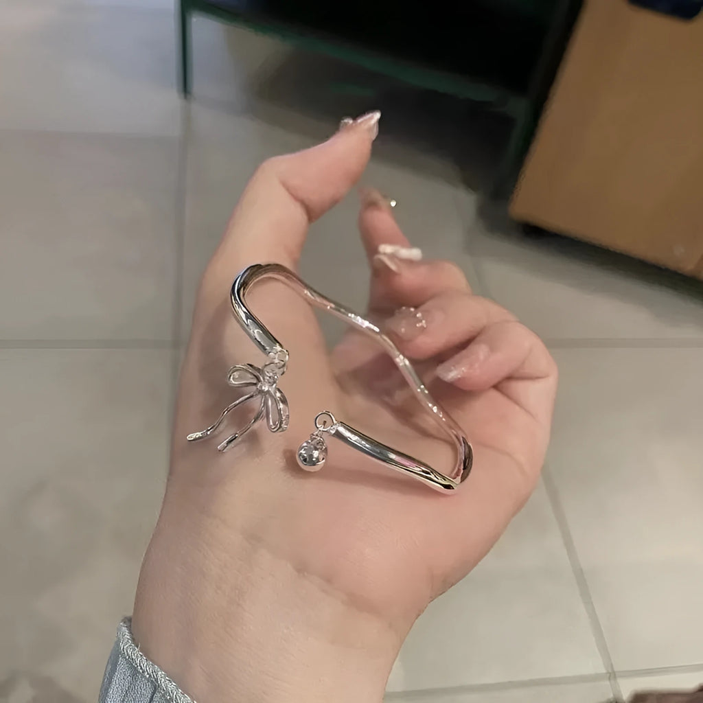 Silver adjustable bracelet with bow and bell charms on wrist showing opening clasp