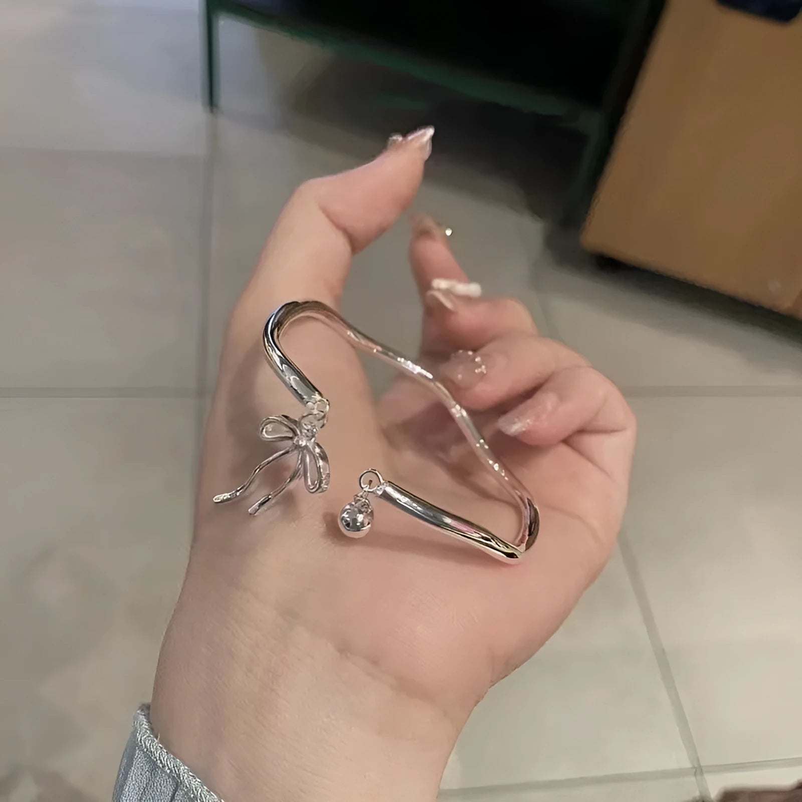 Silver adjustable bracelet with bow and bell charms on wrist showing opening clasp
