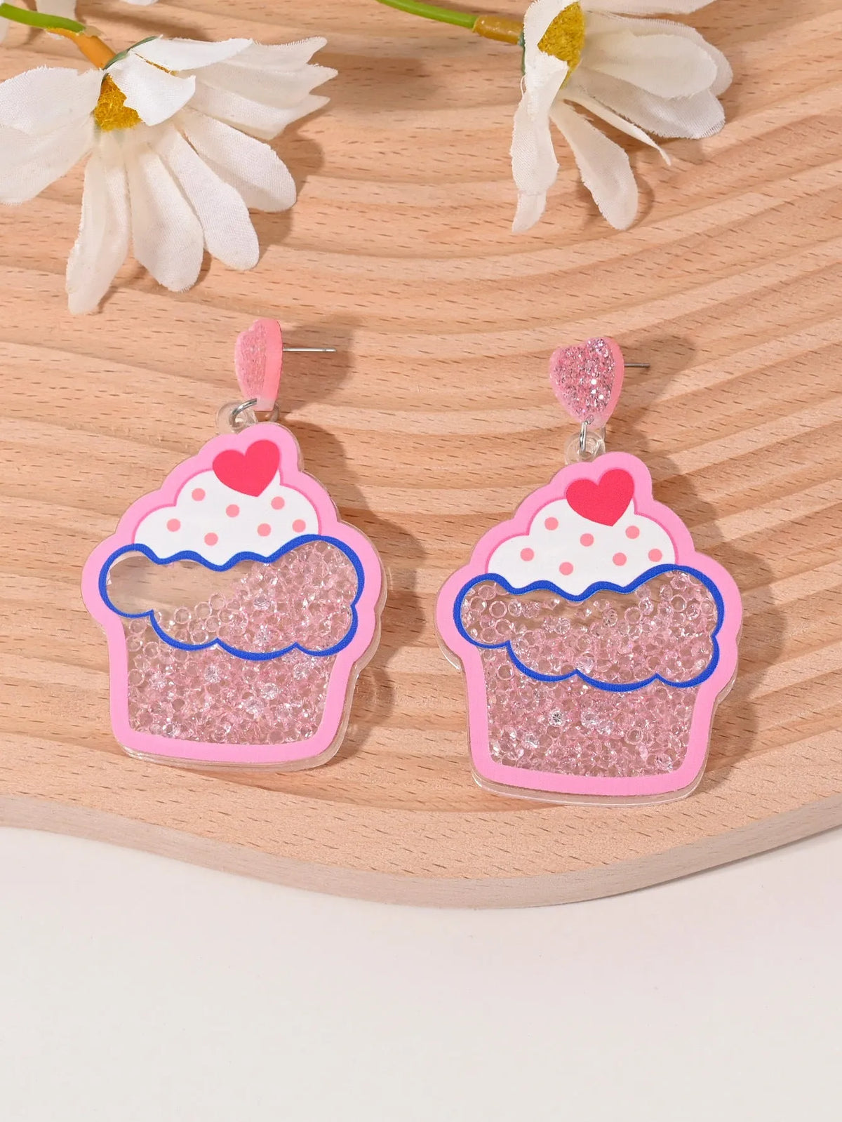 A pair of colourful acrylic earrings with a cake design next to other fruit and ice cream style earrings.