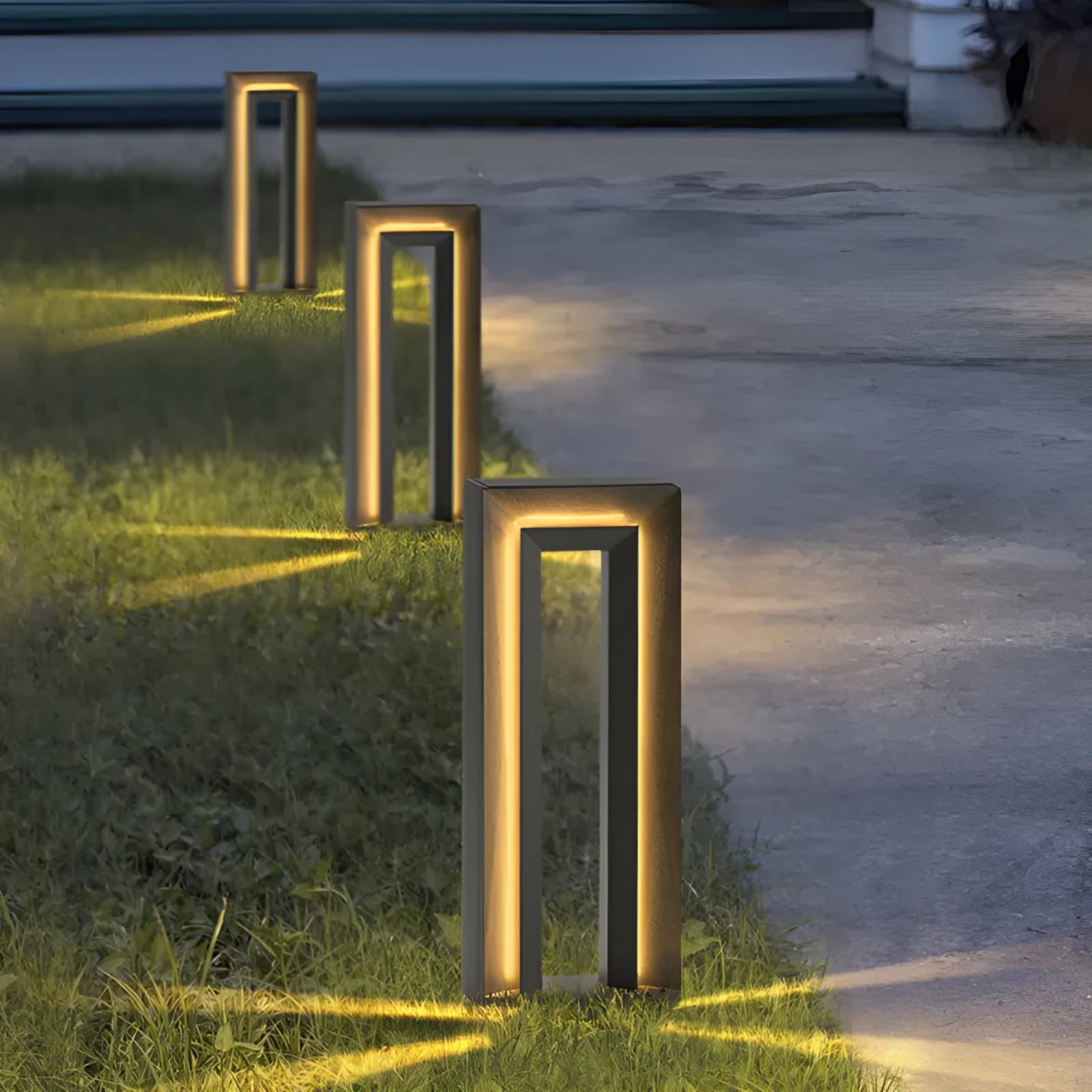 Modern square stainless steel outdoor garden lamp with geometric design on a patio.