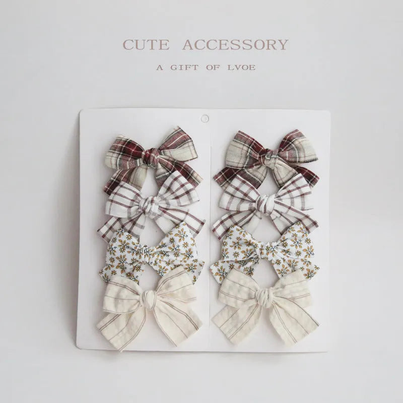 Set of eight children's cloth bow hair clips in various colours including beige polka dot, pink, blue floral, and wine red plaid patterns.
