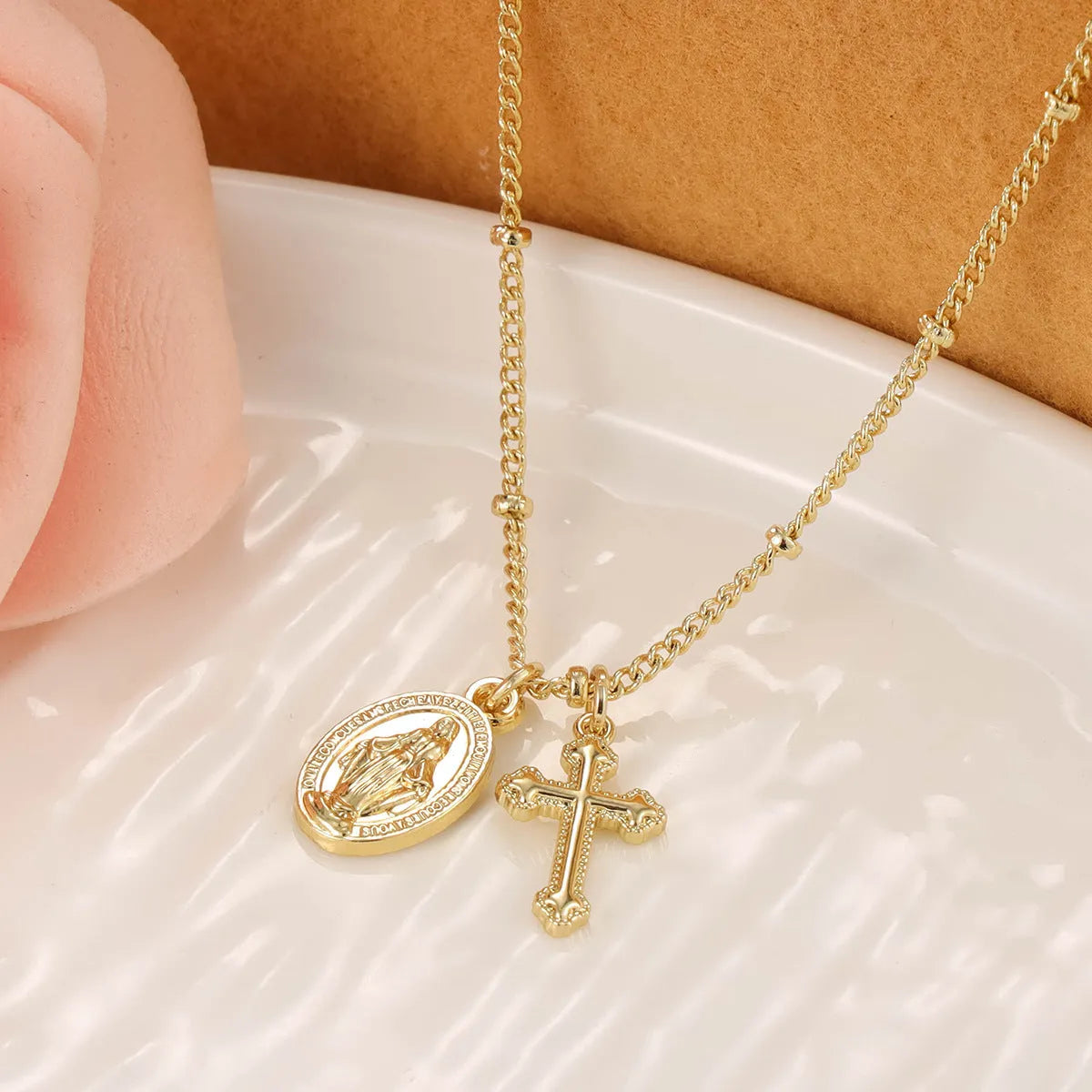 Gold coloured geometric cross Virgin Mary pendant necklace on a chain.