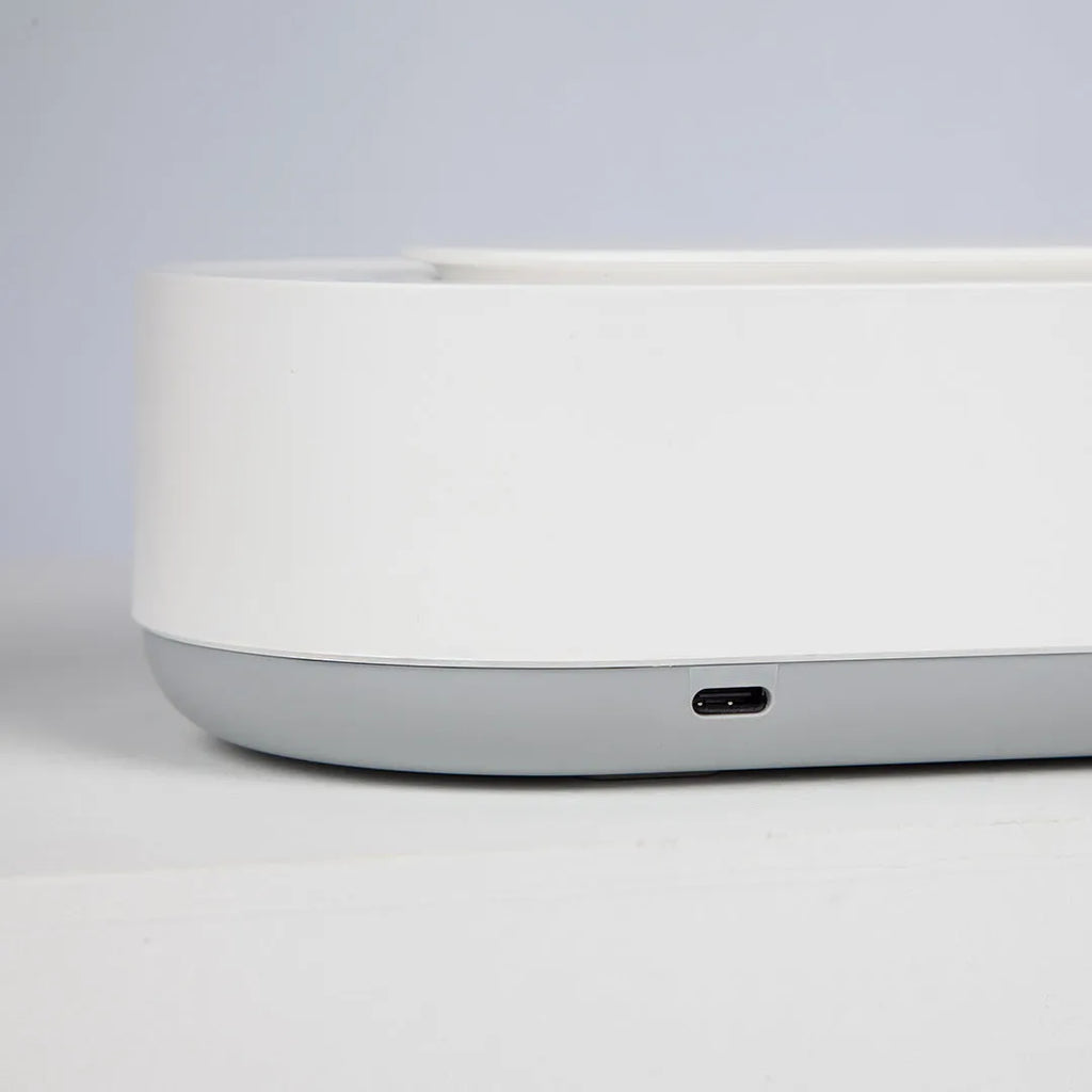 White portable ultrasonic cleaner with touch button next to jewellery and glasses on a table.
