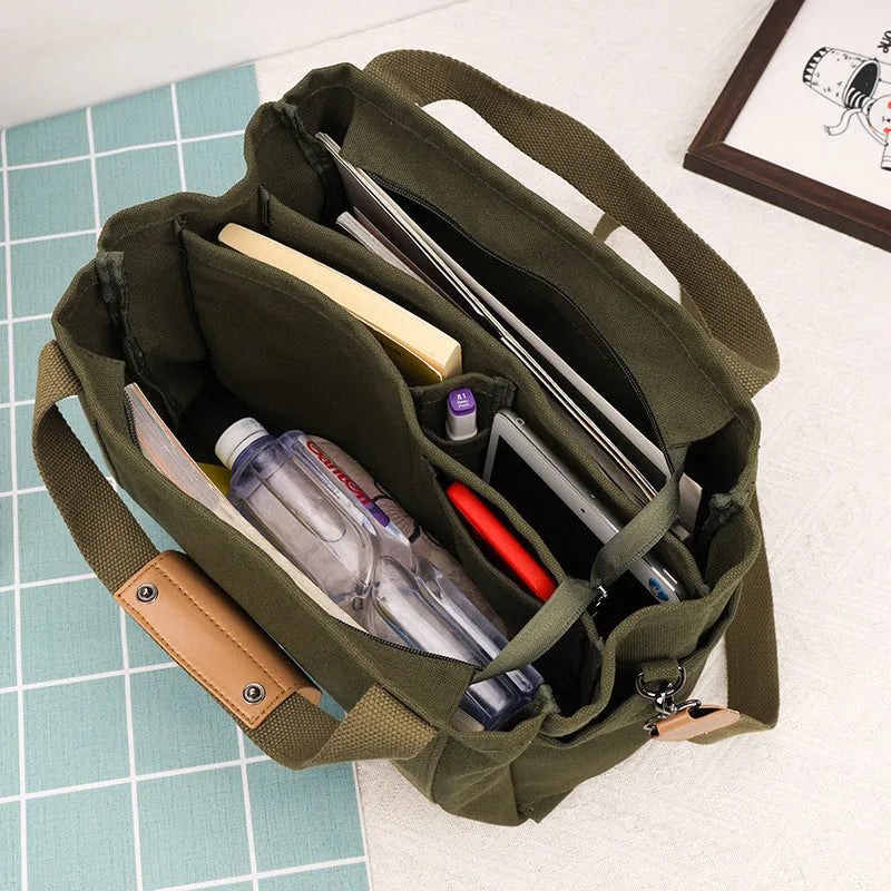 Large horizontal square canvas tote bag with crossbody strap and multiple internal pockets.
