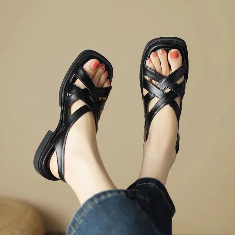 Women's black patent leather beach sandals with square toe and cross-strap design on a light background.
