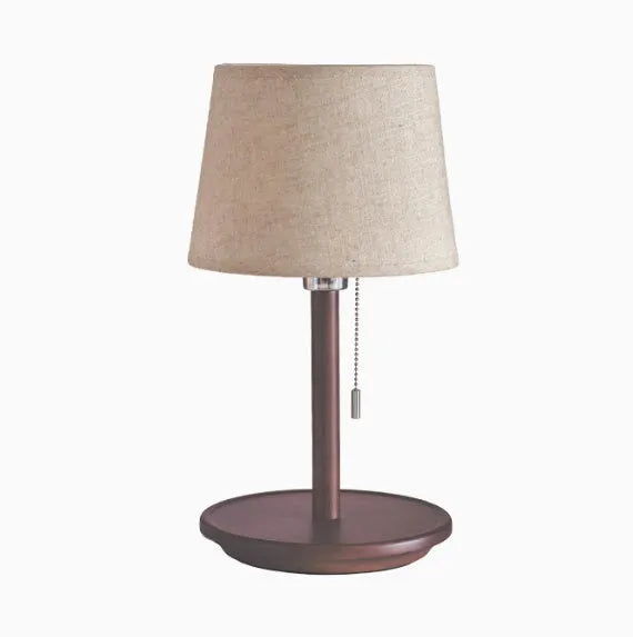 Walnut coloured solid wood bedside lamp with a white cloth shade on a wooden table.