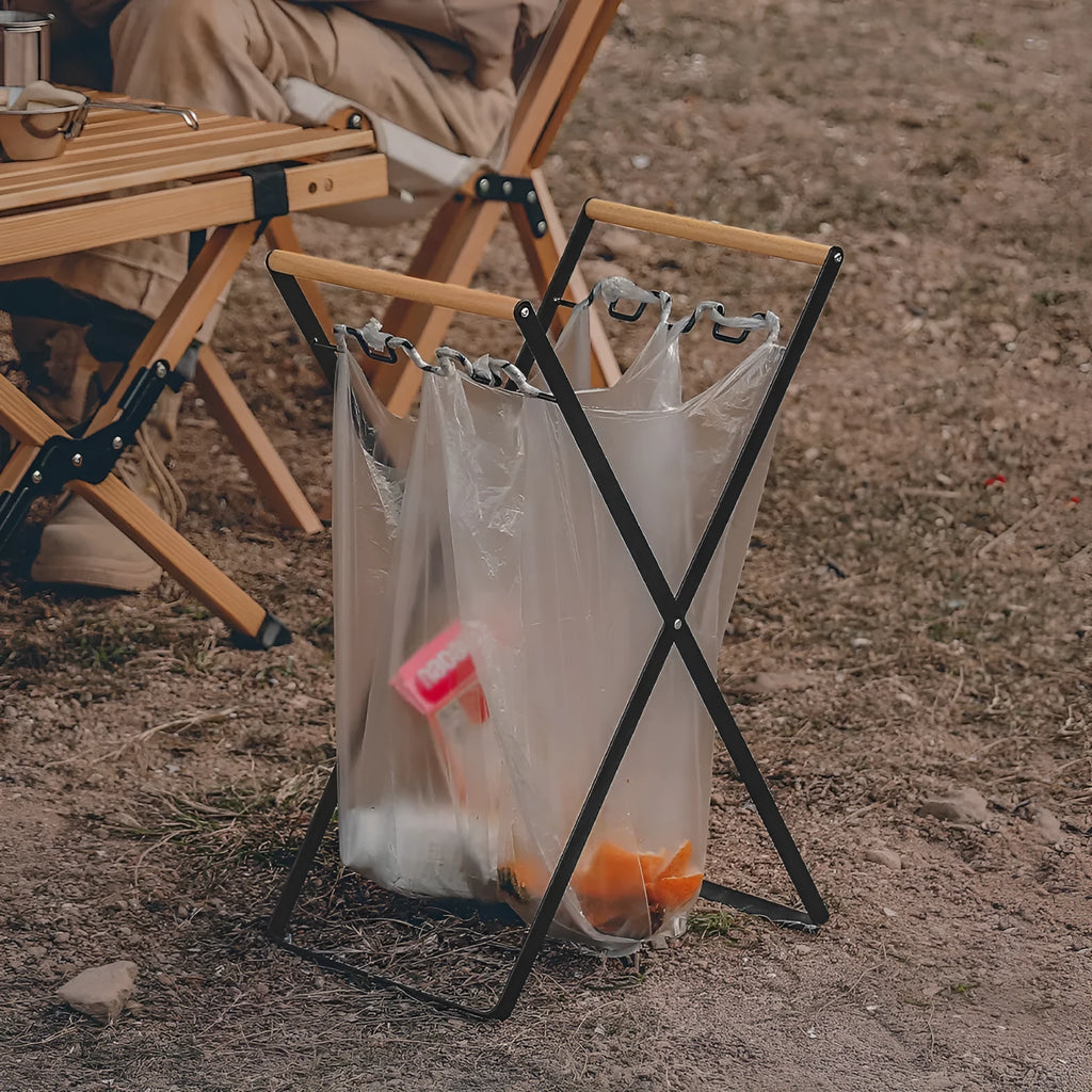 Black folding iron outdoor trash rack with a wooden handle holding a waste bag.