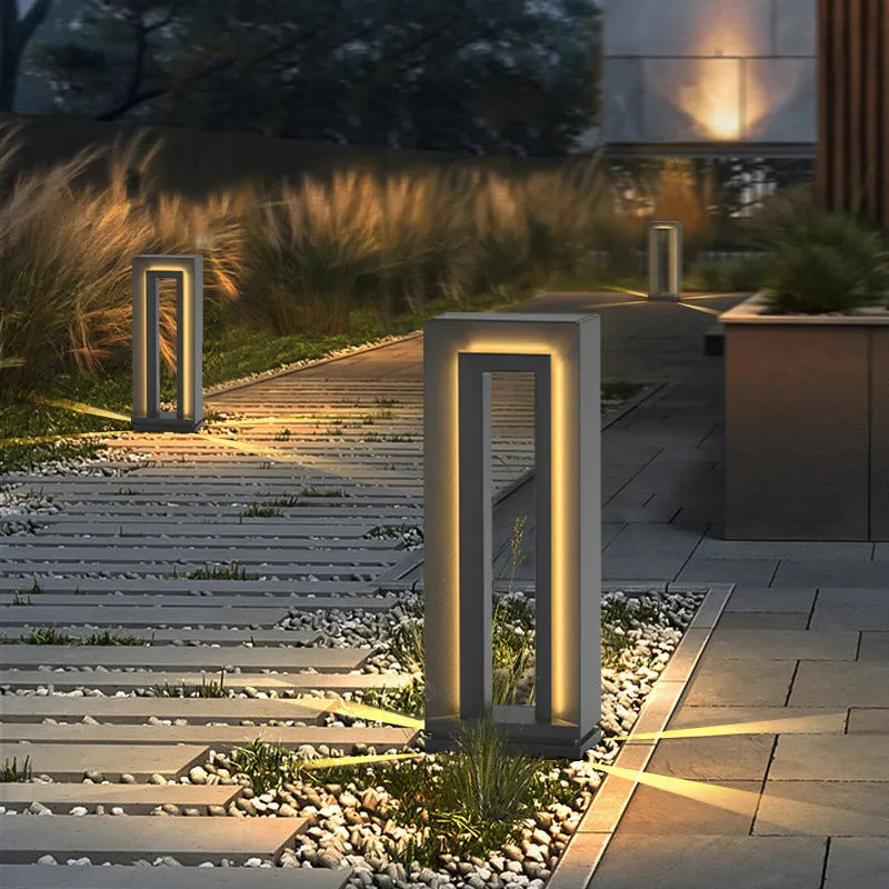 Modern square stainless steel outdoor garden lamp with geometric design on a patio.