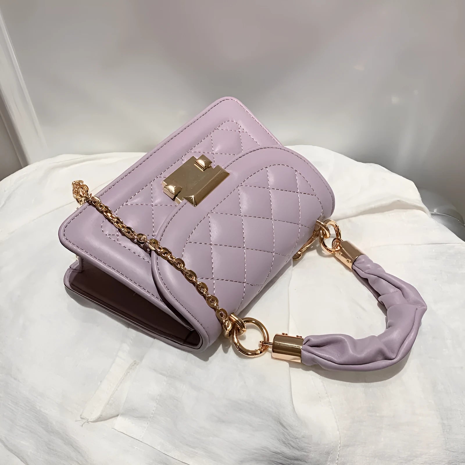 Purple soft PU leather small square shoulder bag with a long strap on a table.