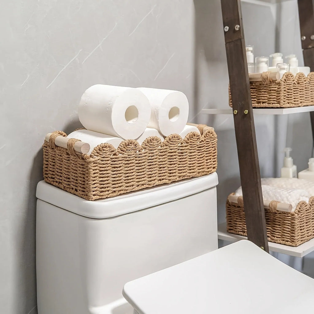 Woven paper storage basket in khaki colour on a wooden desk holding remote controls and pens.