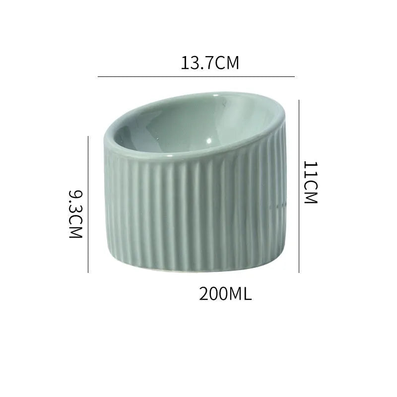 Dark green ceramic elevated cat bowl on a table, showing its raised height and round, tilted shape.